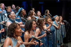 The New York Vocal Collective in performance, singing into microphones in denim