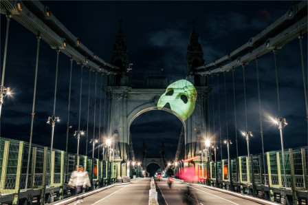 The Phantom of the Opera mask projected onto Hammersmith Bridge in London for the show's 40th anniversary. Photo by Ryan Buchanan