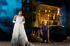 A young woman in a white gown below the open Birling house in An Inspector Calls, 2024 UK touring company. Photo by Mark Douet