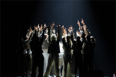 The Boy Blue company massed on a darkened stage with arms raised. Photo by Sophie Bradbury