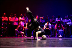 A dancer holds a one-handed freeze in front of a seated crowd at a Boy Blue battle event. Photo by Alex Ferrelly