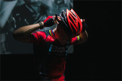 Connor Delves fastening a red cycling helmet in Cadel: Lungs On Legs at Riverside Studios. Photo by Kyle Dax Smith