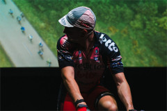 Connor Delves in a cycling cap in front of a projected aerial shot of a race in Cadel: Lungs On Legs at Riverside Studios. Photo by Kyle Dax Smith