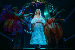 Alice with costumed dancers beneath a floral arch in Cirque Alice, from an earlier staging