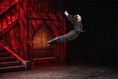 A dancer in mid-leap against a red Gothic set in BIG Live's Dracula