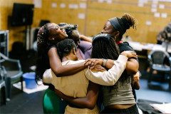 The Girls company in a group embrace during rehearsals