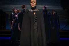 Charlie Burn as Jane, cloaked, with the company behind her. Photo by Victoria Davies