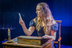 Charlie Burn as Jane reading a letter by candlelight at a writing desk. Photo by Victoria Davies
