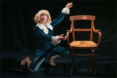 Jordana Belaiche as Little Lord Fondleroy, kneeling beside a wooden chair with one arm raised