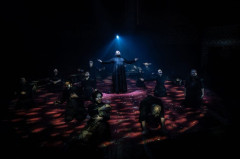 The company of Martin Guerre kneeling in a circle with arms raised around a priest at the Old Vic. Photo by Helen Maybanks