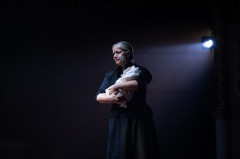 A woman cradles a bundle of white cloth in Martin Guerre. Photo by Helen Maybanks