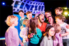 Baffo surrounded by young audience members in On Your Bike Baffo! from OH! Productions. Photo by Paul Blakemore