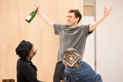 A One Day cast member raises a champagne bottle in rehearsal. Photo by Pamela Raith