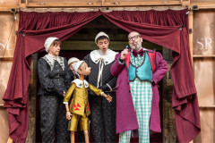 Pinocchio and his puppeteers with a showman in a purple coat, 2025 production at Shakespeare’s Globe. Photo by Johan Persson