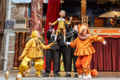 Pinocchio lifted between characters in yellow and orange costumes, 2025 production at Shakespeare’s Globe. Photo by Johan Persson