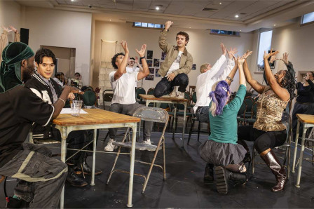 The company of Rent in rehearsal, with Gaten Matarazzo standing on a table. Photo by Pamela Raith