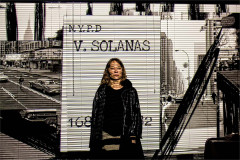 Emily Woof in front of a projected N.Y.P.D. mugshot board reading V. Solanas in Revolver. Photo by Sheila Burnett