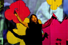 Emily Woof with her arms raised against a projection of pop-art flowers in Revolver. Photo by Sheila Burnett