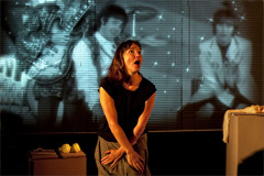 Emily Woof against a projected black-and-white image of a band on stage in Revolver. Photo by Sheila Burnett