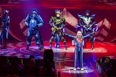 A young cast member stands before three engines under red light in Starlight Express at the Troubadour Wembley Park Theatre. Photo by Pamela Raith