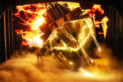 A vast structure breaks apart in fire and forked lightning above a fogbound stage, two figures below it. Photo by Matthew Murphy and Evan Zimmerman