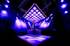 A lone figure stands on top of the banquette beneath the suspended grid of light panels on Amy Jane Cook’s set for Table 17. Photo by Steve Gregson