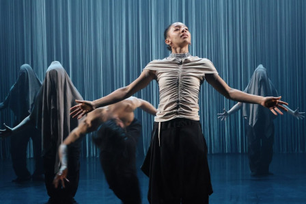 A dancer stands with arms spread wide in front of shrouded figures and a curtain of strings in Dickson Mbi Company's Tellus at Sadler's Wells East