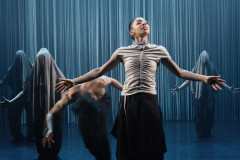 A dancer stands with arms spread wide in front of shrouded figures and a curtain of strings in Dickson Mbi Company's Tellus at Sadler's Wells East