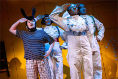 A donkey in a striped T-shirt salutes alongside three astronauts in white flight suits in Toto at Polka Theatre