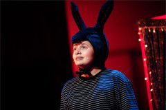 A donkey in a striped T-shirt looks up under a red light in Toto at Polka Theatre