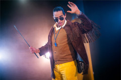 A character in sunglasses and a fringed suede jacket brandishes a cane in Toto at Polka Theatre