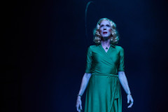 A performer in a green dress in a pool of blue light in The Law of Mayhem