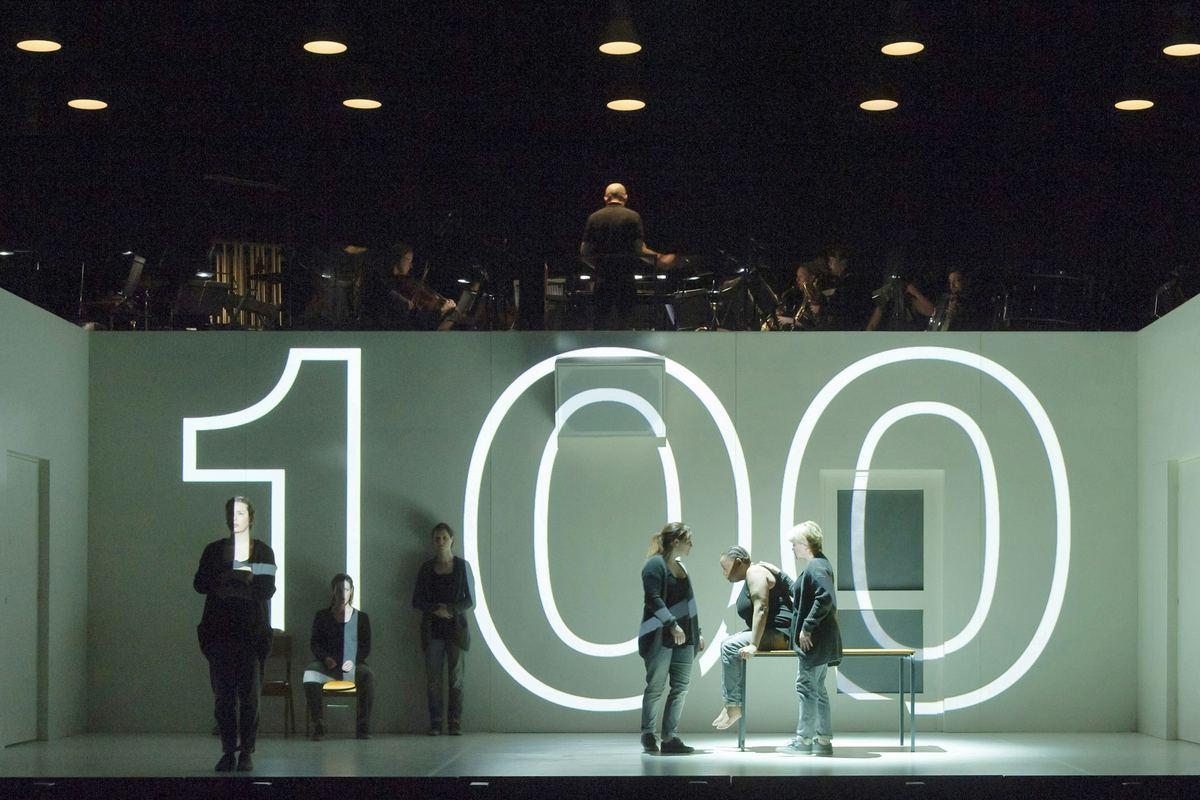 A projected 100 fills the white set of 4.48 Psychosis, with the Chroma Ensemble in the gallery above, in the 2016 Royal Opera staging
