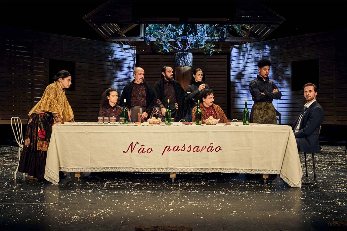 The full company of Catarina and the Beauty of Killing Fascists gathered behind the family table beneath the cork oak