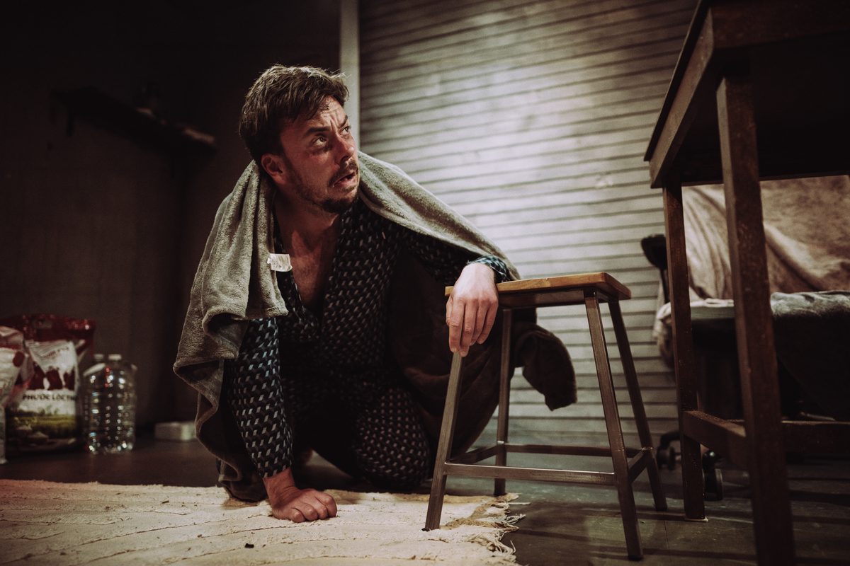 Ross Gaynor as Ashton crouched in the bunker in A Slow Fire at Jermyn Street Theatre