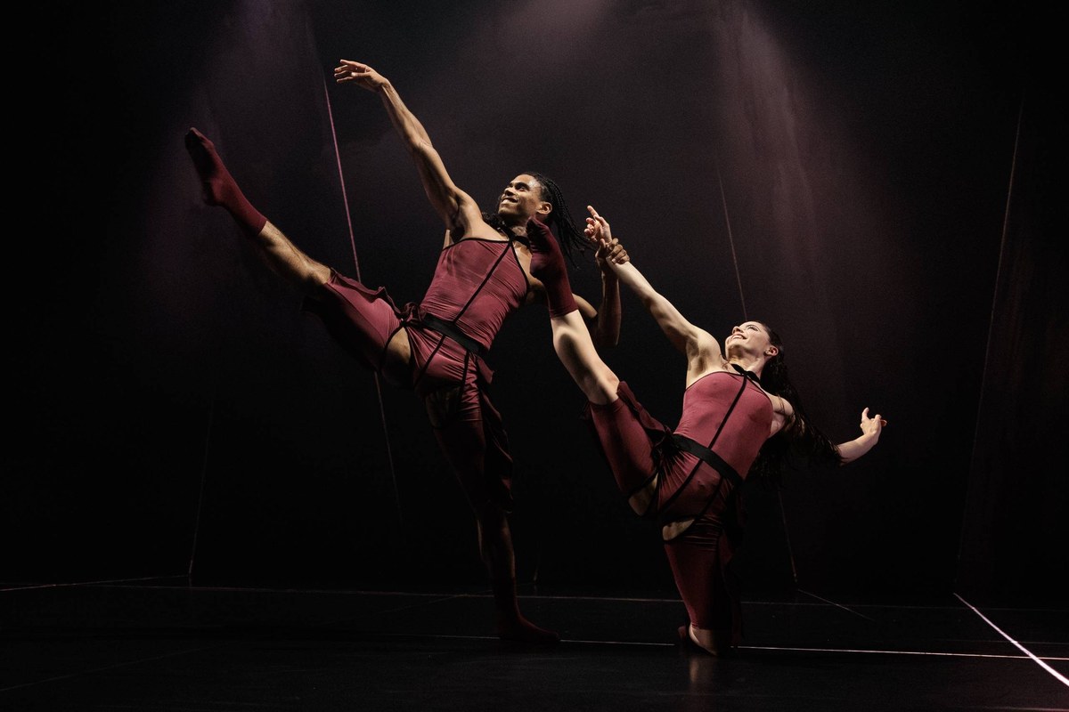 Two Acosta Danza dancers in burgundy costumes extend their legs high in Pearls in Cuban Baroque at Sadler’s Wells