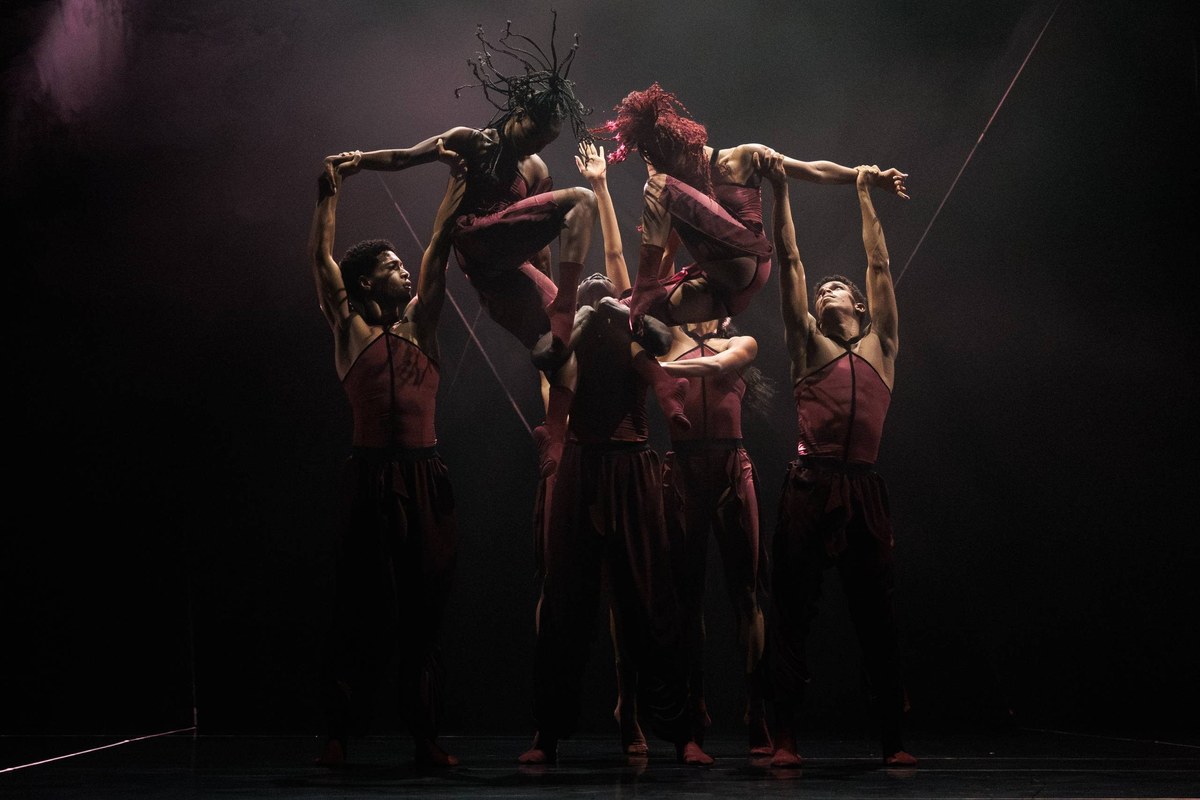 A tight group of Acosta Danza dancers in burgundy reach upwards in Pearls in Cuban Baroque
