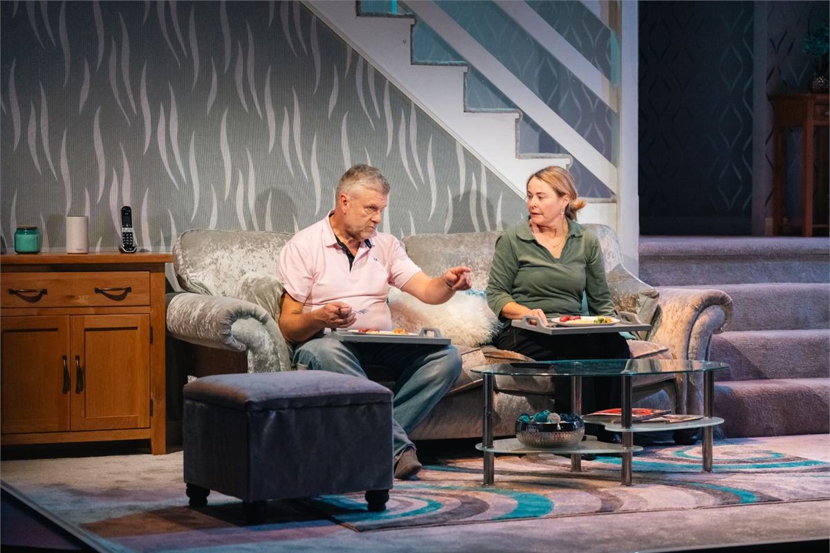 Phil Corbitt and Sarah Belcher eat dinner on the sofa in All at Sea at Live Theatre, Newcastle. Photo by Von Fox Promotions