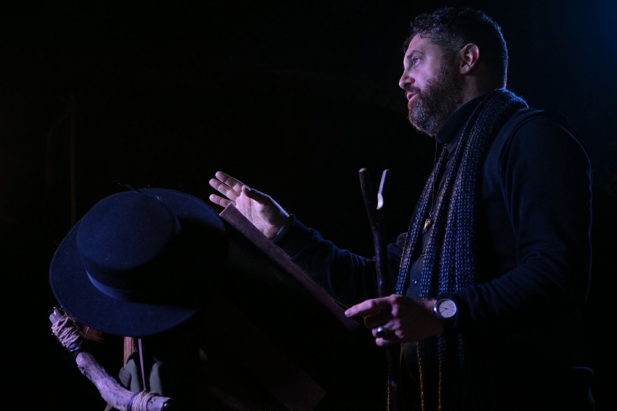 Dov Citron at a lectern in Animal Farm: As Witnessed by Moses the Raven at Barons Court Theatre