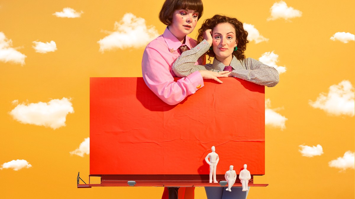 Key art for Zoo Co's Three Men On A Billboard: two performers lean on a blank red billboard against a yellow sky, with three tiny figures standing on the gantry below