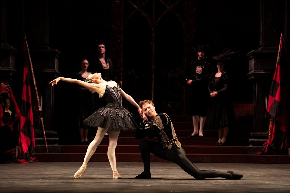 Odile in a black tutu leans back over a kneeling Prince Siegfried in the ballroom scene of Birmingham Royal Ballet's Swan Lake Odile in a black tutu leans back over a kneeling Prince Siegfried in the ballroom scene of Birmingham Royal Ballet's Swan Lake