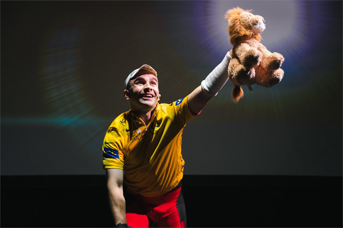 Connor Delves in the yellow jersey, holding a toy lion aloft in Cadel: Lungs On Legs at Riverside Studios. Photo by Kyle Dax Smith