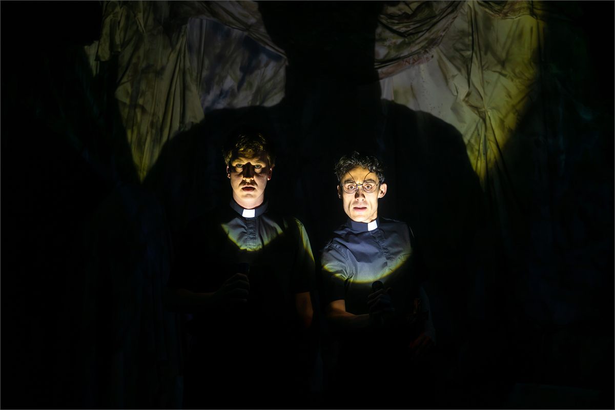 Two of the Crybabies trio lit by torchlight in priests' collars in The Scaring. Photo by Mihaela Bodlovic