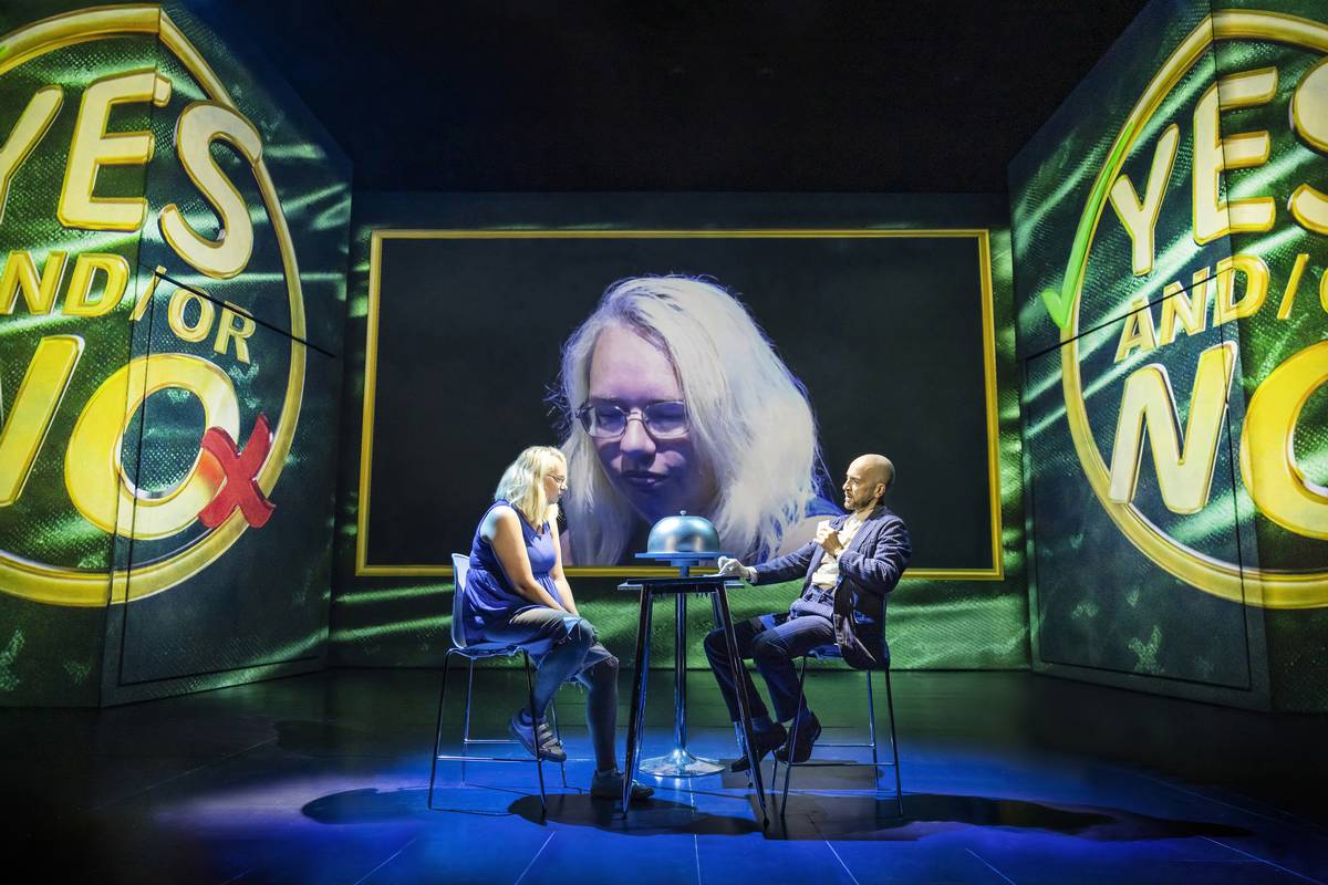Derren Brown with an audience volunteer at a table in front of a giant YES AND/OR NO screen in Only Human at the Apollo Theatre