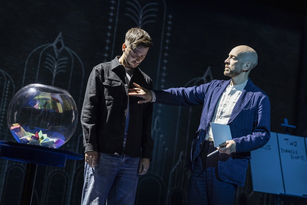Derren Brown with his hand on the shoulder of an audience volunteer beside a goldfish bowl of folded papers in Only Human