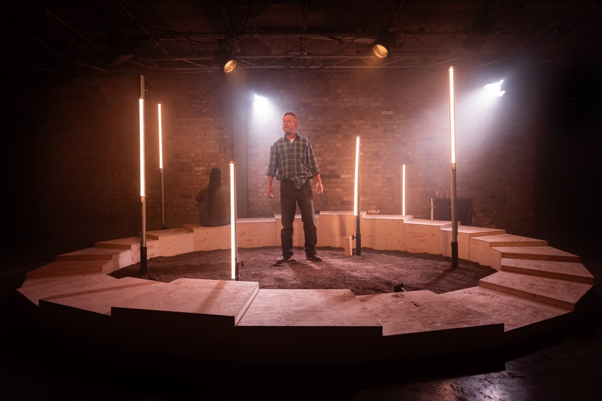 Chris Simmons as Eddie stands inside the lit circle of Peiyao Wang’s set for Fire Fire