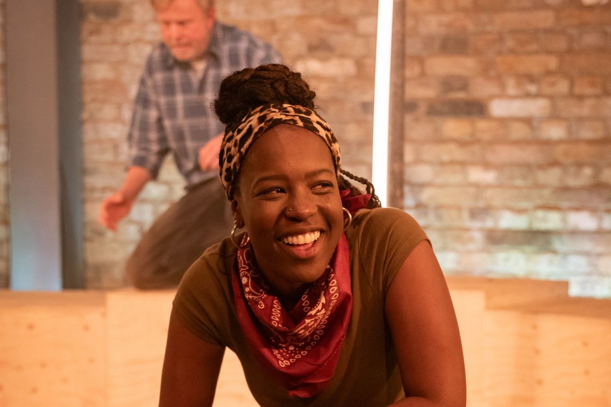 Gabrielle Brooks as Paige laughing, with Chris Simmons as Eddie behind her, in Fire Fire