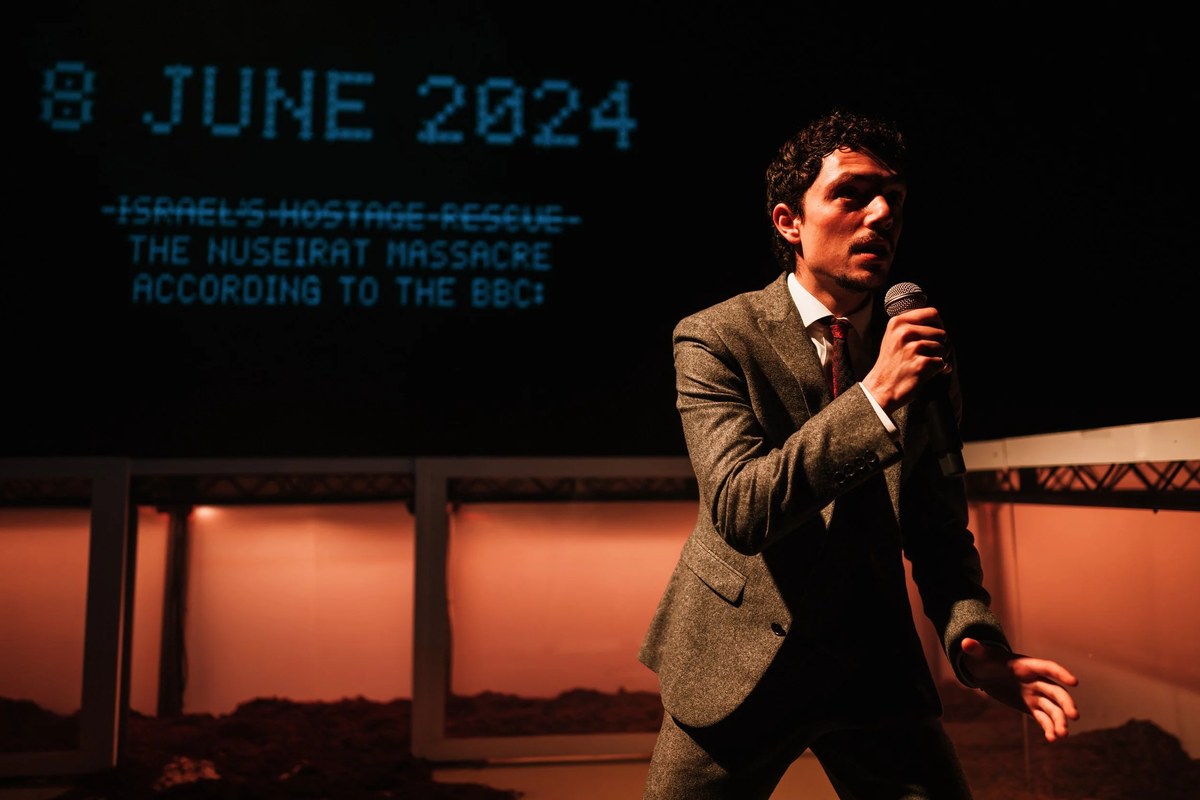 Luca Kamleh Chapman with a microphone in The First Year (of the Gaza Genocide in the Media) at New Diorama Theatre. Photo by Alex Brenner