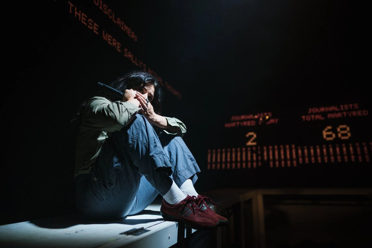 A lone performer beside the running totals projected in The First Year (of the Gaza Genocide in the Media). Photo by Alex Brenner