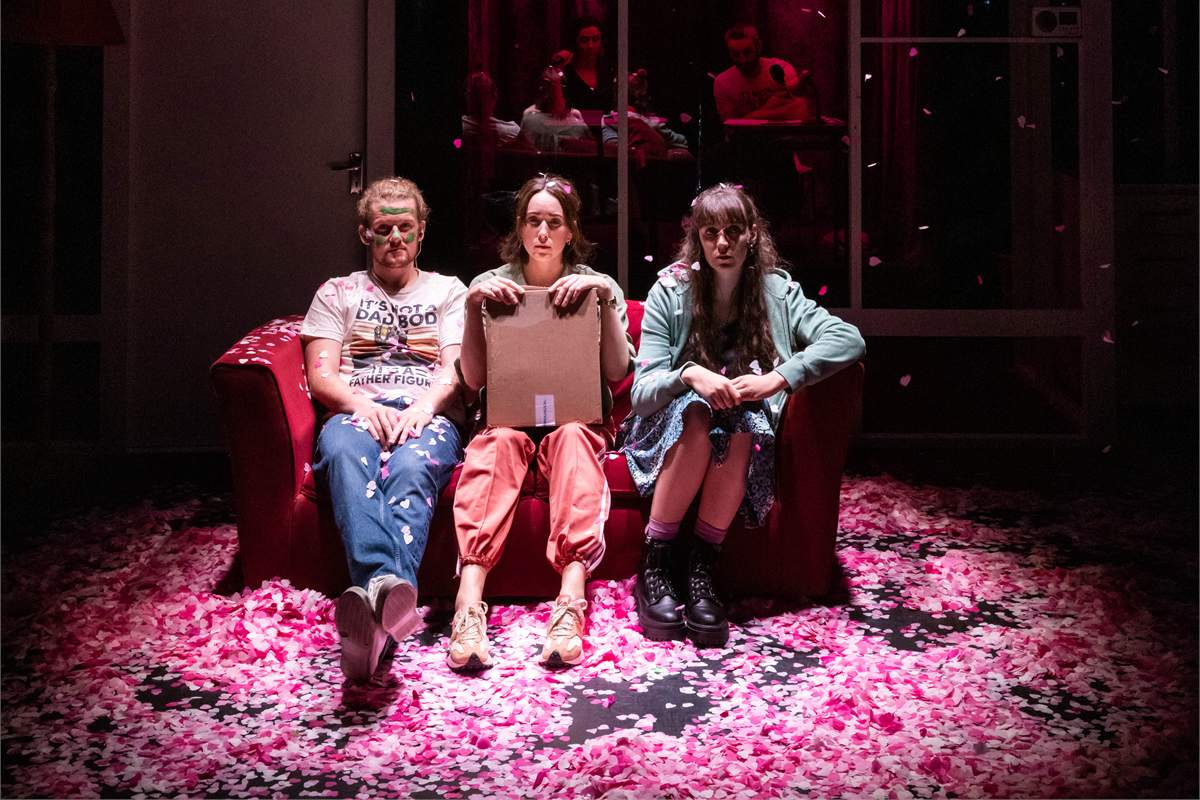 A scene from Dead Centre’s Good Sex, three performers on a red sofa amid a carpet of pink petals. Photo by Ste Murray